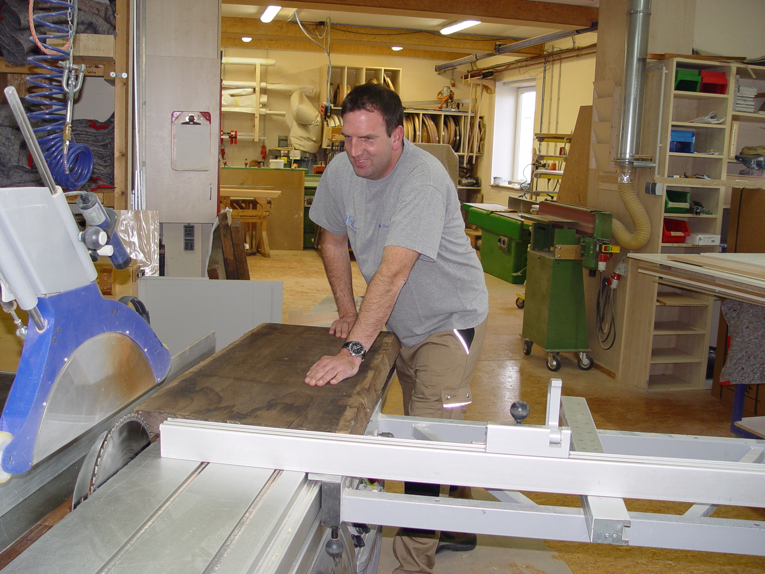 Mann bedient Kreissäge in einer Werkstatt, schneidet ein Holzbrett.