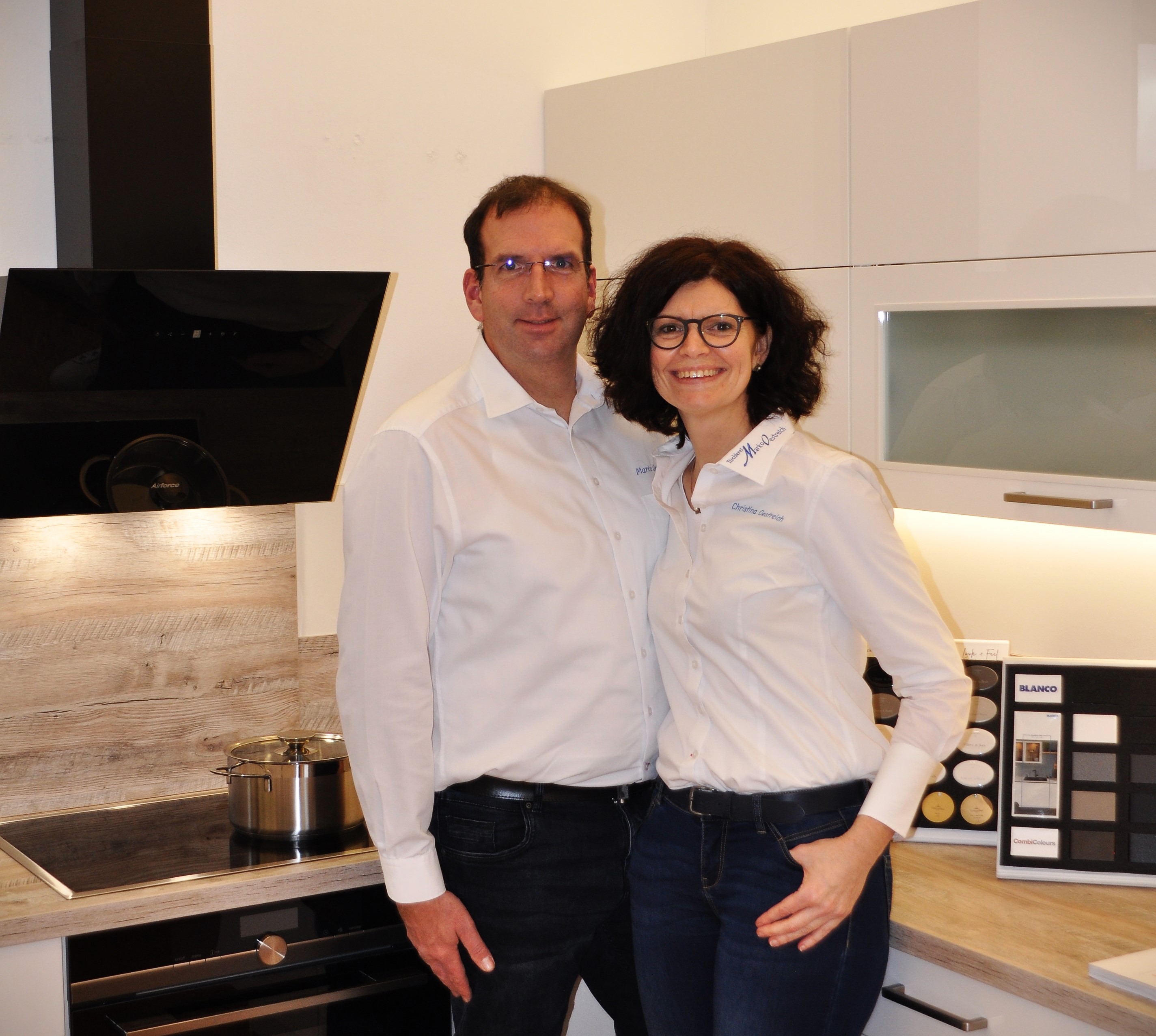 Mann und Frau lächeln gemeinsam in einer modernen Küche, beide tragen weiße Hemden.