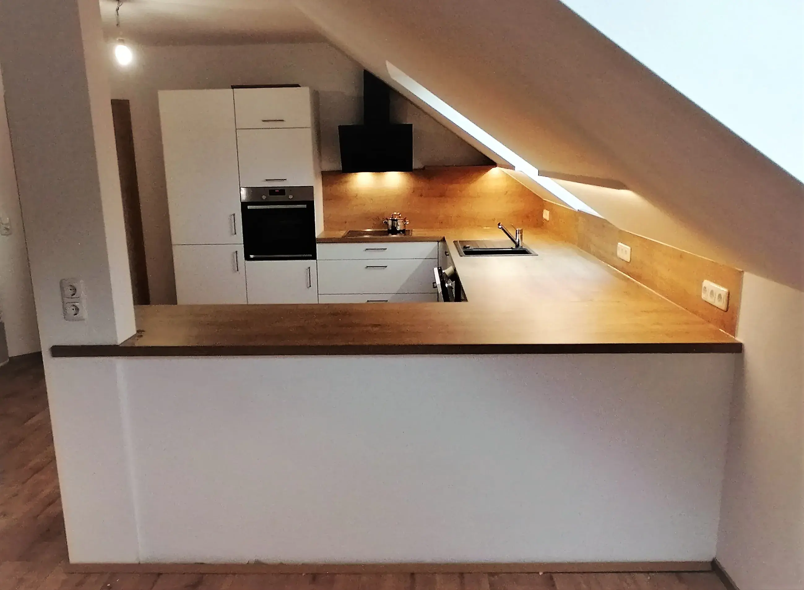 Moderne Einbauküche mit Holzarbeitsplatte unter einer Dachschräge.