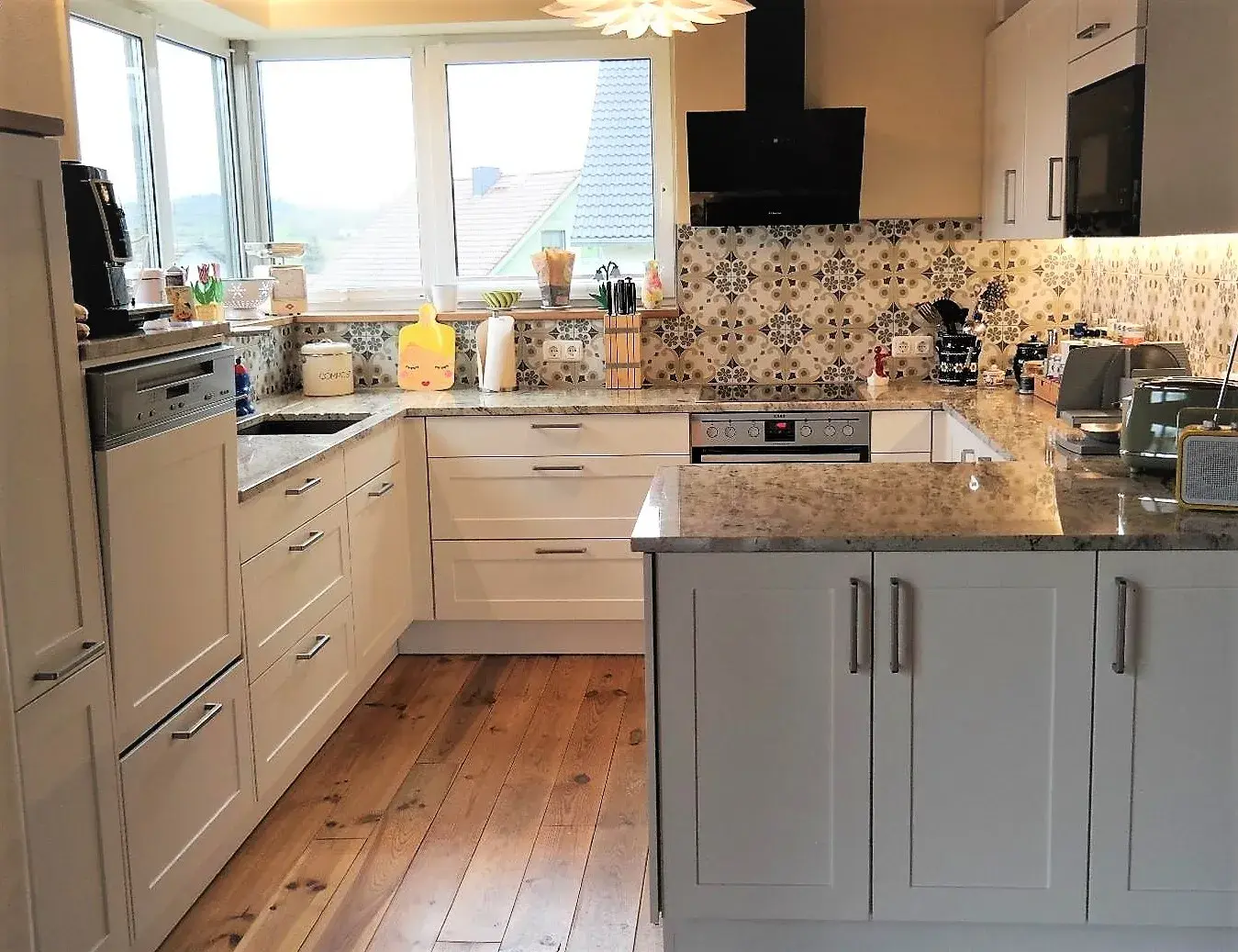 Moderne Küche mit weißen Schränken, Holzfußboden und gemusterten Fliesen.