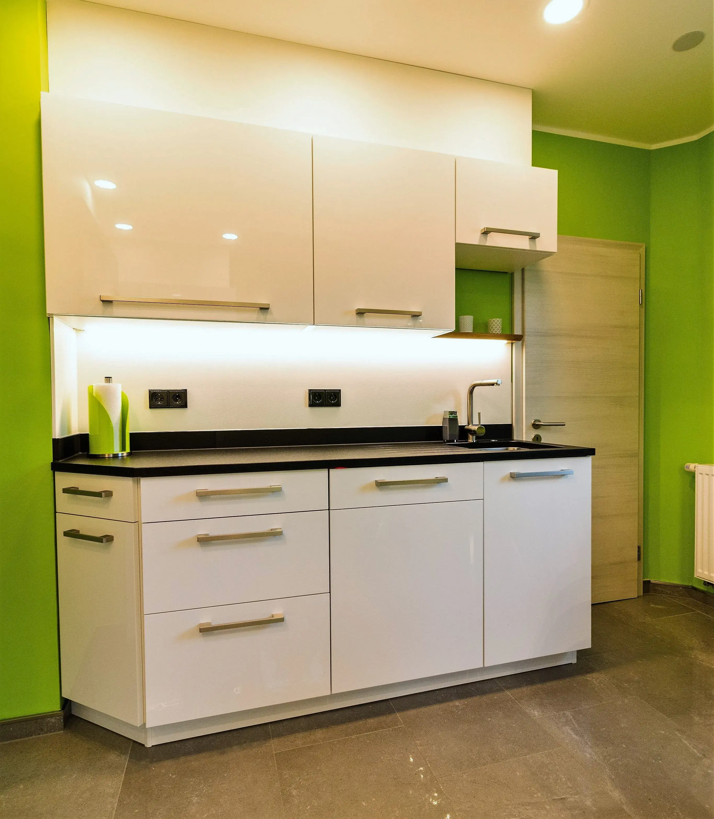 Moderne weiße Küche mit grüner Wand und schwarzer Arbeitsplatte