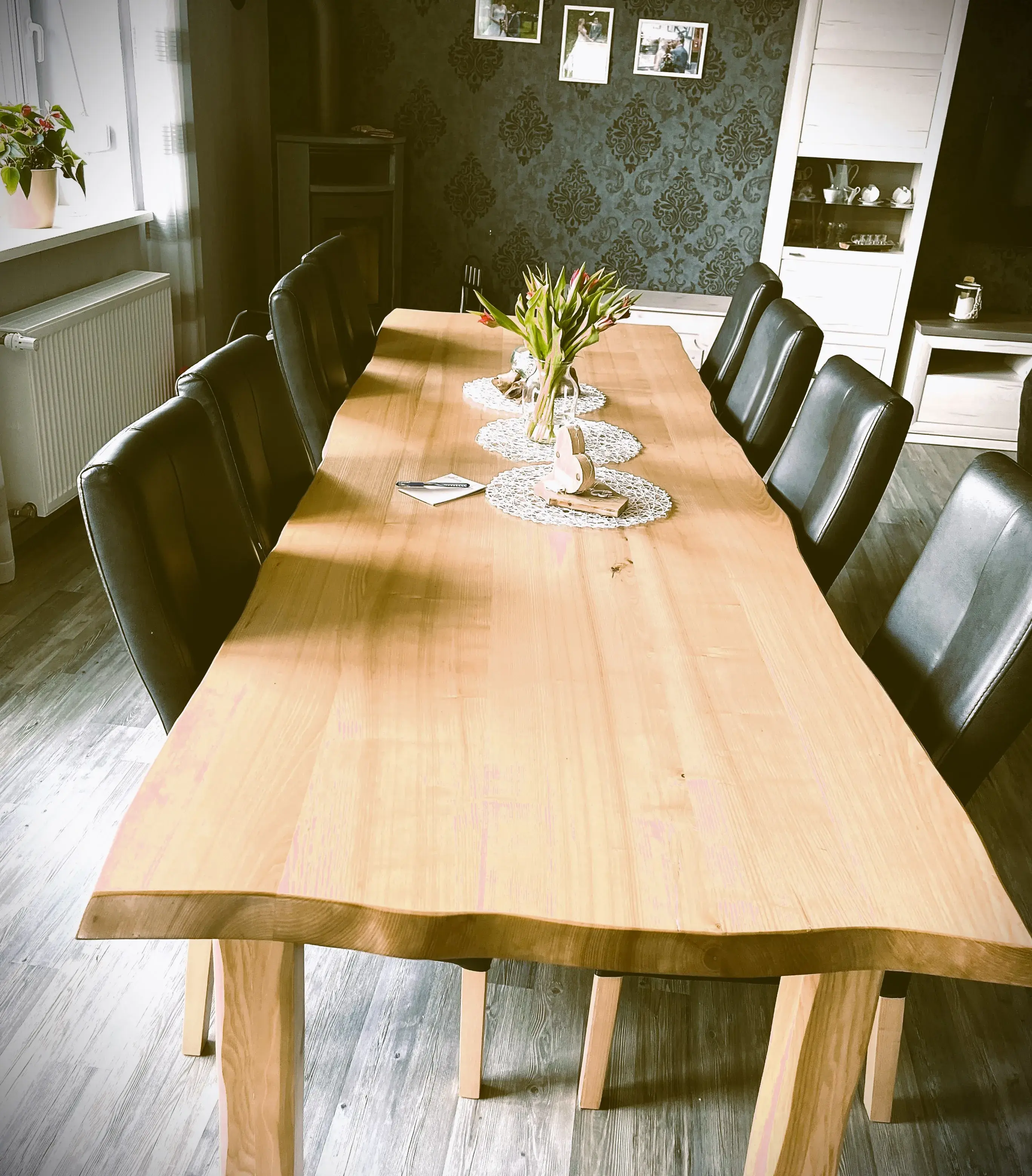 Langer Holztisch mit schwarzen Stühlen, Vase mit Blumen in der Mitte, Wohnzimmerumgebung.