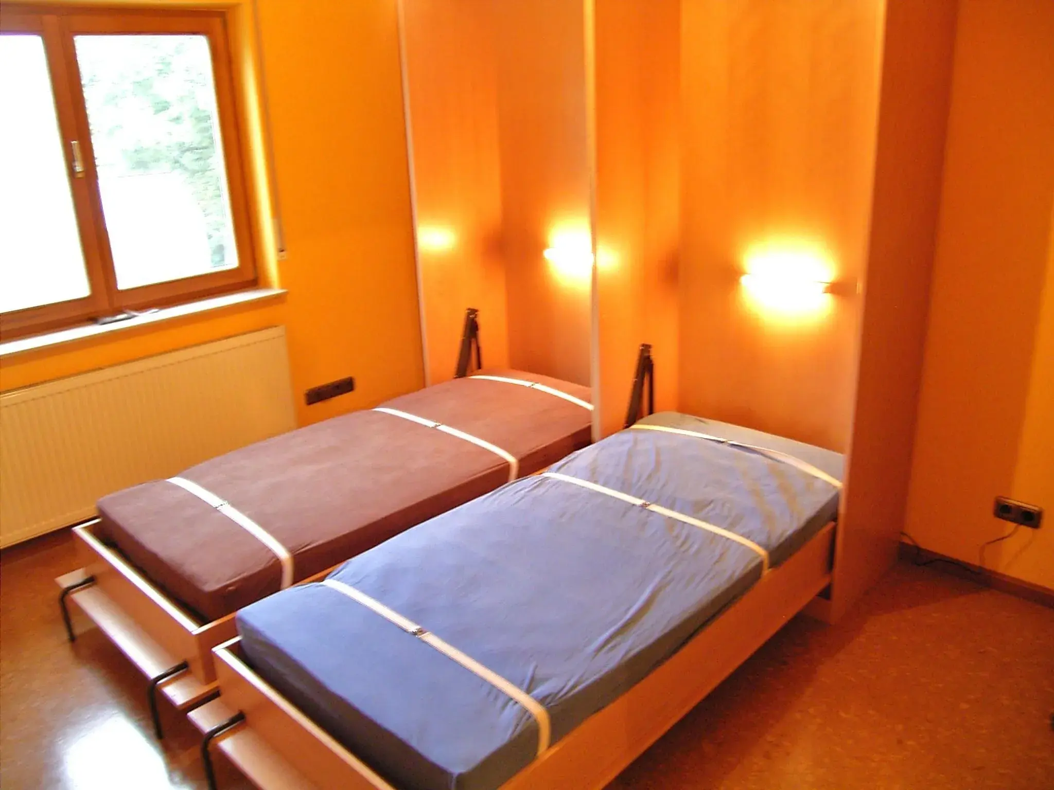 Zwei Einzelbetten mit bunten Bezügen in einem orange gestrichenen Zimmer.