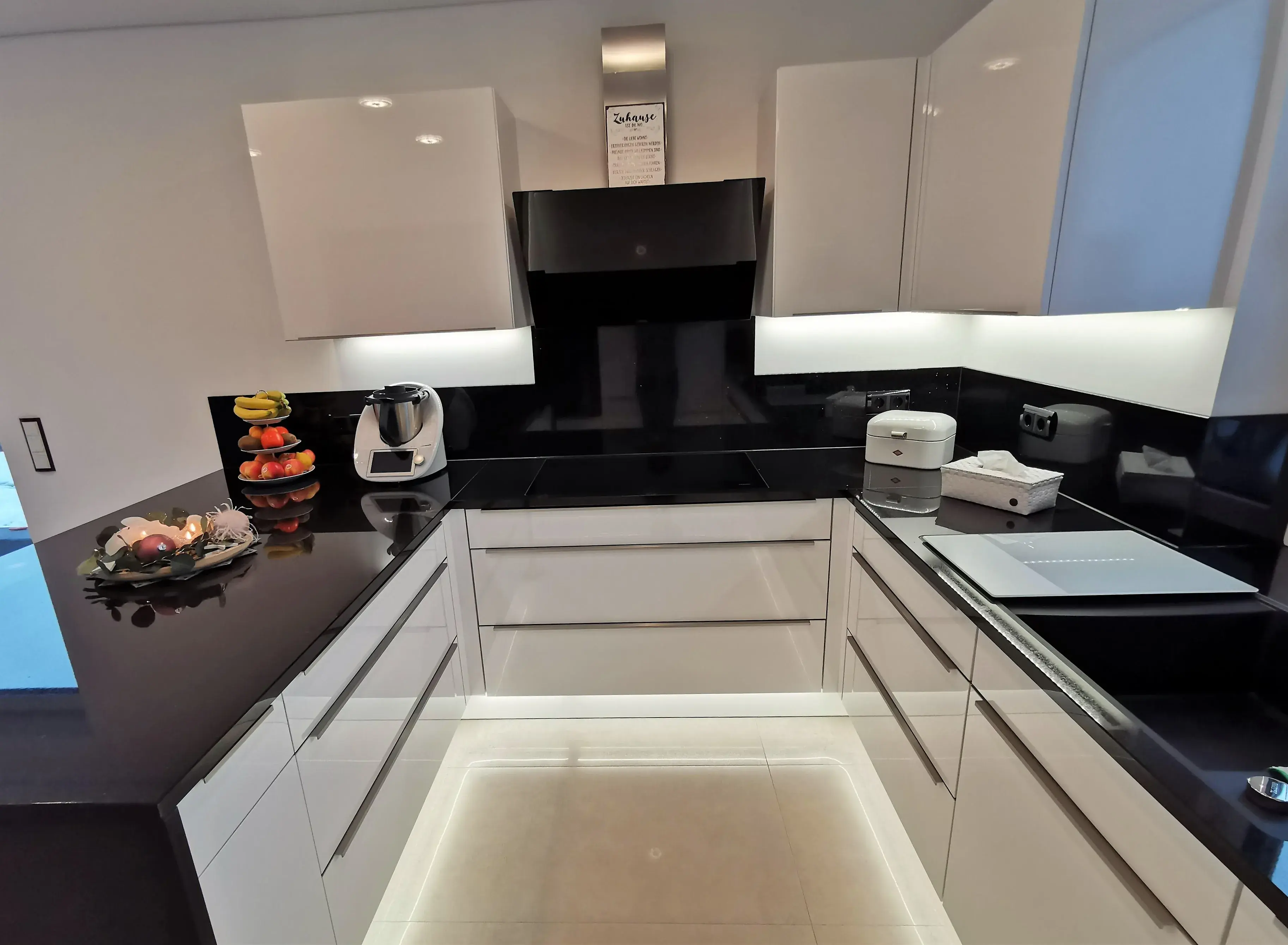 Moderne weiße Küche mit glänzenden schwarzen Arbeitsplatten und kleinen Küchengeräten.