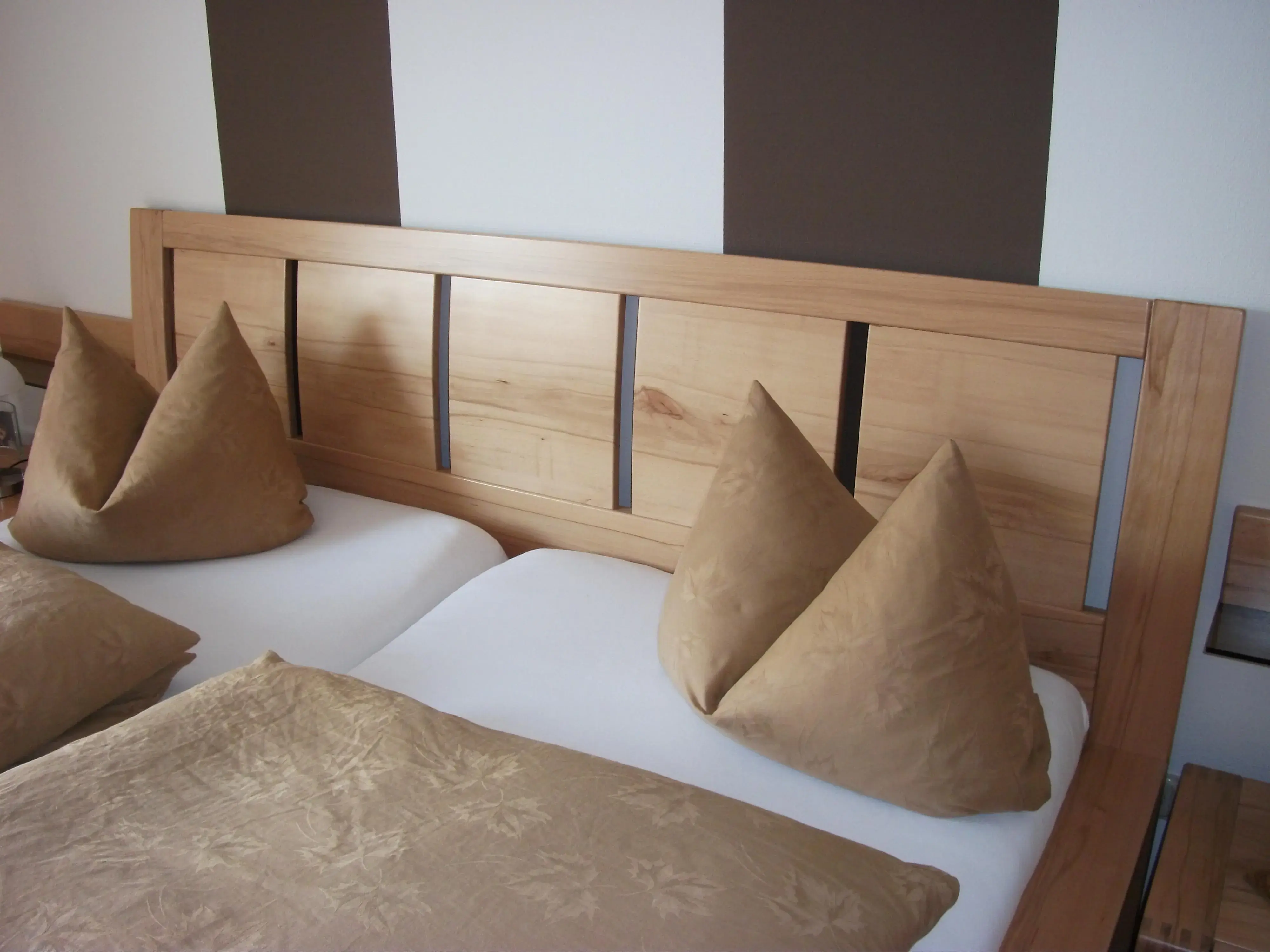 Doppelbett mit brauner Bettwäsche und Kissen vor einem Holzkopfteil.