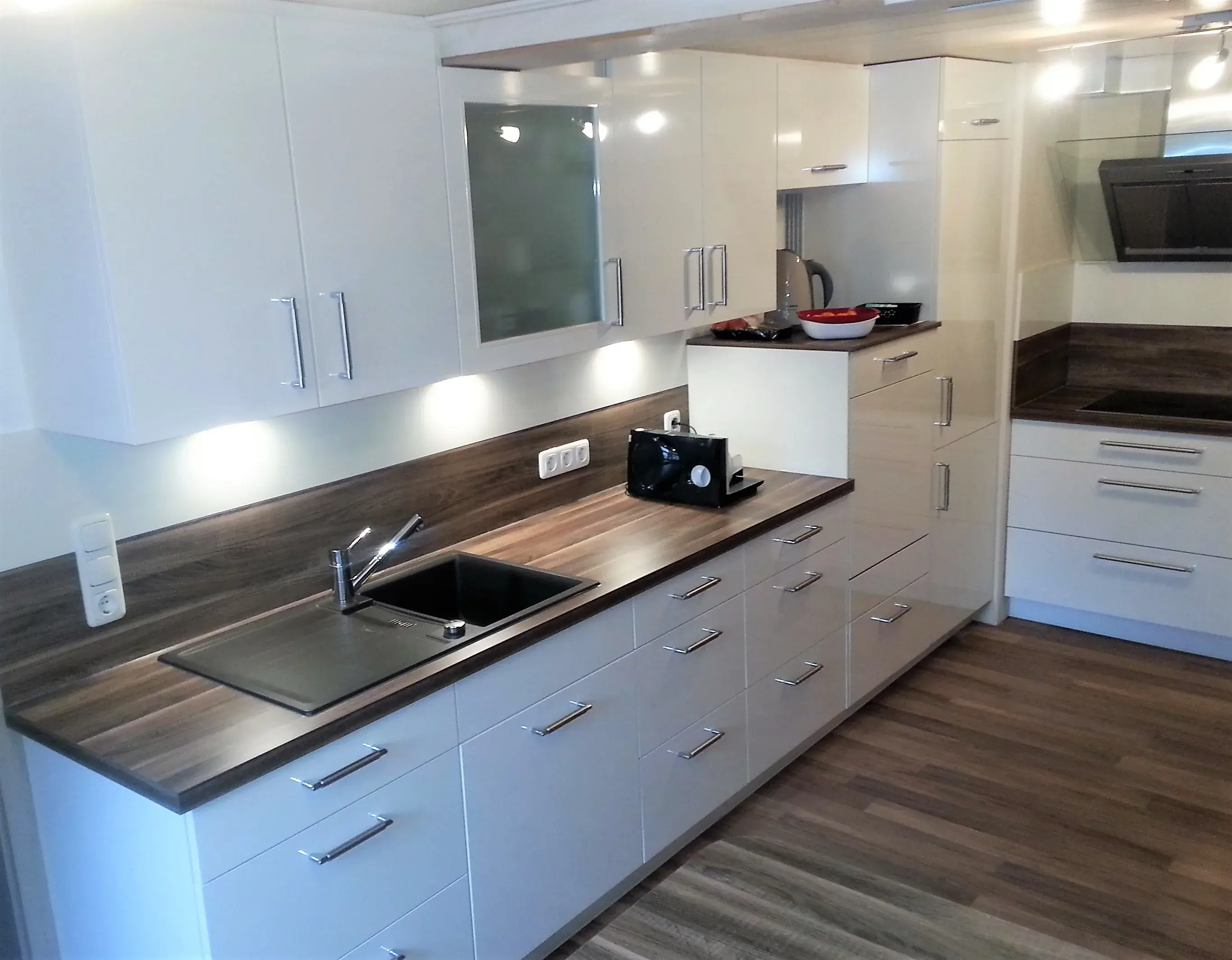 Moderne weiße Einbauküche mit Holzarbeitsplatte und Unterbaubeleuchtung