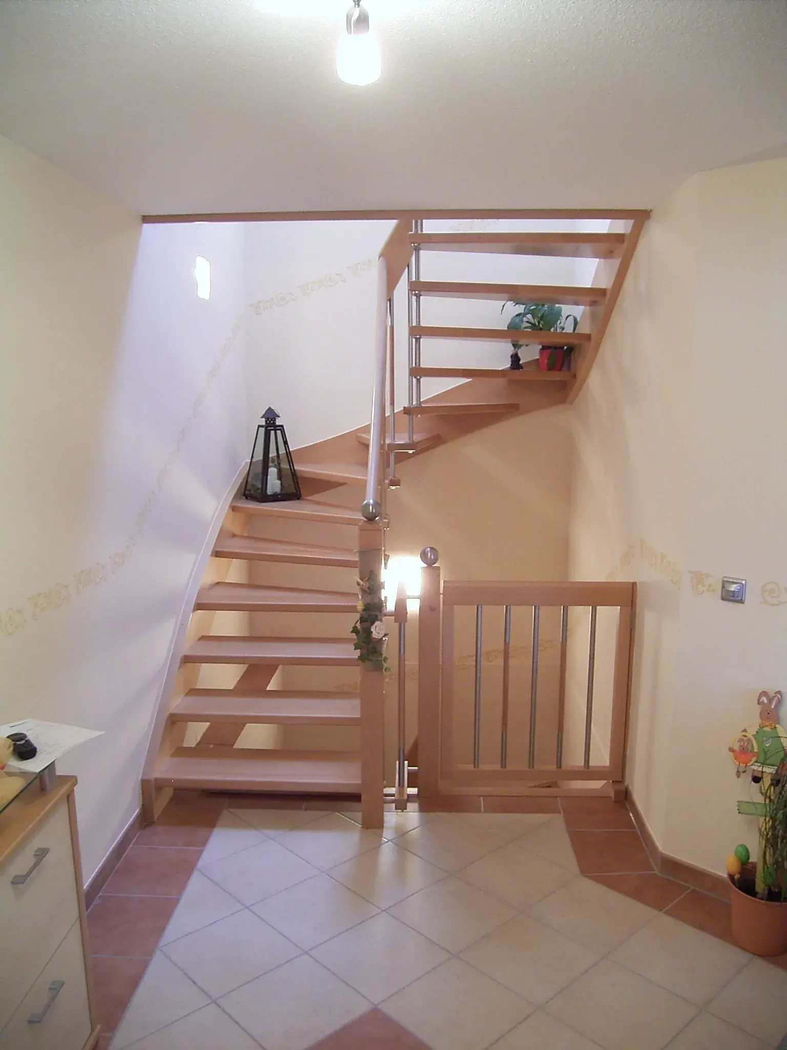 Hölzerne Treppe in einem hellen Flur, Pflanze und Laterne auf dem Treppenabsatz.